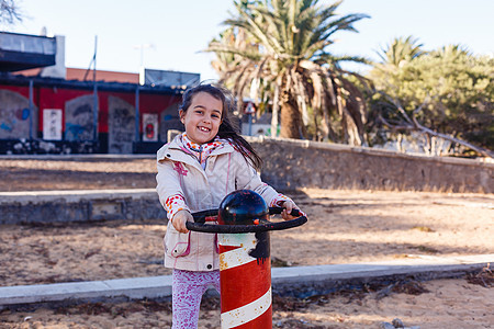 可爱的小女孩在游乐园里 拿着轮船方向盘娱乐微笑裙子队长魅力帽子小姑娘玩具车轮水手图片