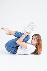 穿着T恤衫和牛仔裤的年轻caucasia女孩举起她的腿 跪着图片