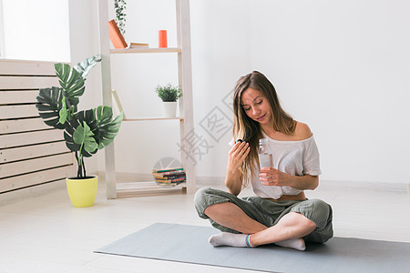 年轻美丽的女孩在垫子上练瑜伽 休息时喝着饮用水 健康 健康的生活方式概念训练身体运动装女性运动培训师瓶子房间运动员有氧运动图片