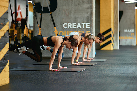 3名年青运动妇女在健身房用Trx健身带锻炼全时参加体操图片