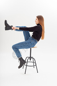 身穿黑色高领 蓝色牛仔裤的年轻有吸引力的caucasia女人穿上靴子天幕成人冒充女性女士青年椅子金发姿势毛衣图片