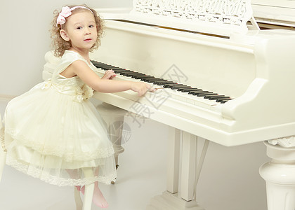 美丽的小女孩在用白色大钢琴弹琴音乐裙子音乐会钢琴家艺术潮人房间乐器音乐家童年图片