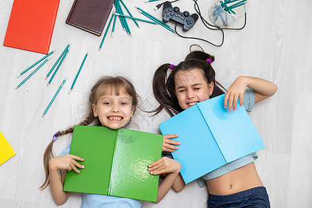 两个小女孩姐妹 读一本书躺在地板上写着评书女孩姐姐教育孩子们快乐地面学习地毯乐趣图片