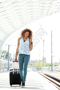 带着手机和手提箱在车站行走的全身微笑的年轻女子图片