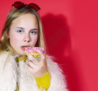 可爱的金发少女摆出时尚风格 红色背景的甜甜圈 生活方式人们的观念饮食小吃垃圾美丽快乐重量乐趣女士发型女孩图片