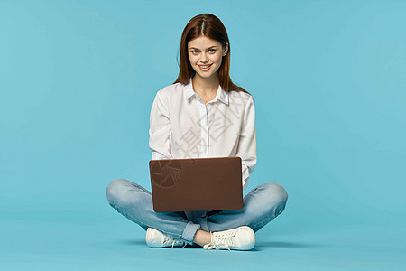 拥有手提笔记本电脑的妇女坐在地板学习互联网技术的蓝背景蓝色成人女孩女士药片商业青少年红色学生白色图片