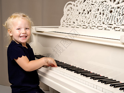 美丽的小女孩在用白色大钢琴弹琴学习音乐家钥匙孩子乐器交响乐教育房间艺术键盘图片
