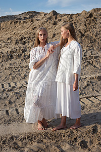 两位有吸引力的年轻姐妹 穿着优雅白色衣服在采沙场上摆着高雅白衣双胞胎女性沙坑青少年女士采砂冒充头发金发女郎裙子图片