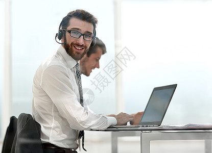 手持耳机的商务人士坐在办公桌旁推销员电话职场商业成人电脑窗户经理合作工作图片