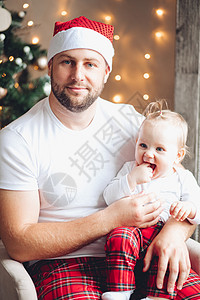 英俊的年轻爸爸在圣诞节气氛中 抱着一个婴儿跪在自己的膝上图片
