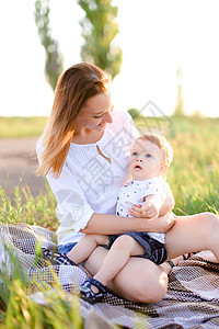 年轻的天主教母亲和小孩坐在草坪上 在背景的草地上图片