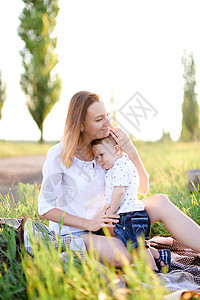 年轻的欧洲母亲 带着小孩坐在格子上 在背景的草地上图片