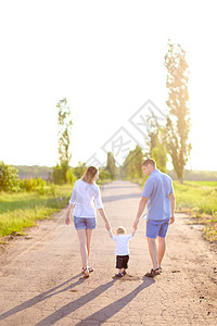 妈妈抱着儿子年轻妈妈和父亲带着小宝宝在路上行走 阳光灿烂的天气闲暇父母幸福孩子母亲儿子阴影成人阳光短裤背景