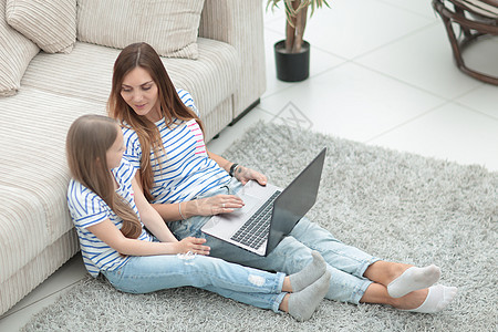母亲和女儿坐在一个舒适的起居室中的地板上教学手表沙发娱乐笔记本互联网公寓女孩快乐父母图片