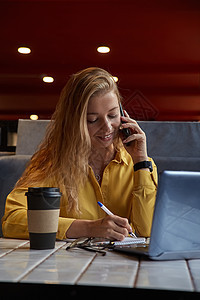 坐在咖啡店的年轻 身穿盛装的卡瓦西安青年妇女 由智能手机打电话杯子写作技术咖啡女士职场自由职业者饭馆商业电脑图片