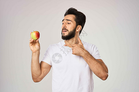 穿着白色T恤的快乐男子 在健康水果手里拿着苹果 带着苹果乐趣男性沙拉盘子微笑蔬菜市场玉米店铺食物图片
