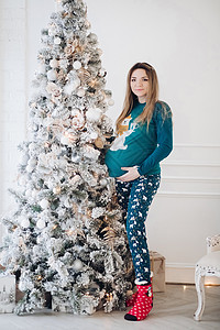 穿着睡衣的有吸引力的孕妇在圣诞节树附近出现图片