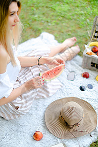 金发美女坐在水果和帽子边上 吃西瓜 草在背景中图片