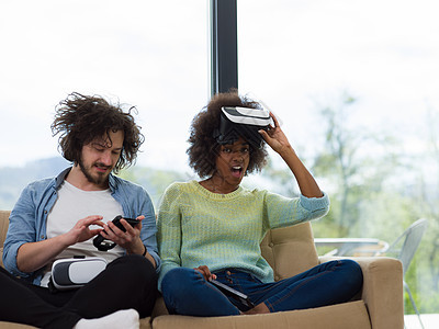 使用虚拟现实耳机的多种族夫妇技术沙发乐趣房间黑色视频模拟活动眼镜手表图片