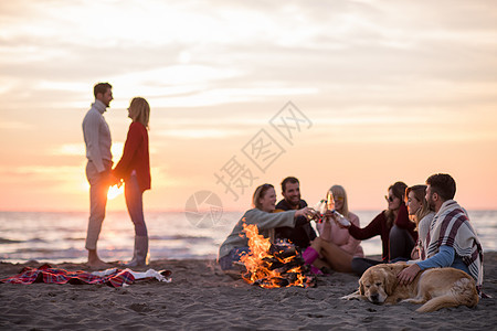 在海滩日落时和朋友共度欢乐的情侣休闲友谊火焰营火女性乐趣篝火动作衣服幸福图片