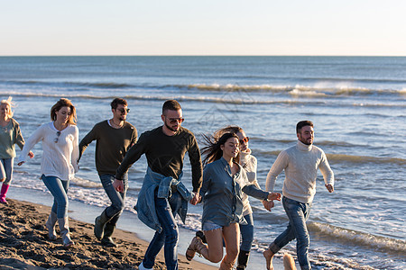 秋天在海滩上奔跑的一群朋友海岸情侣年轻人鹅卵石服装帽子假期朋友们跑步海岸线图片