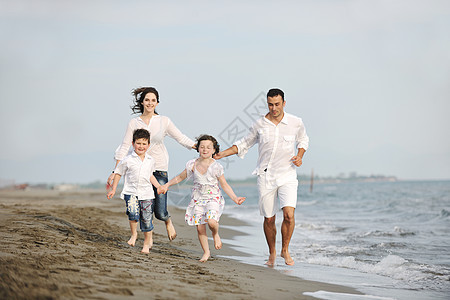 快乐的年轻家庭在海滩上玩得开心父母父亲旅行女孩儿子喜悦女士童年跑步天空图片