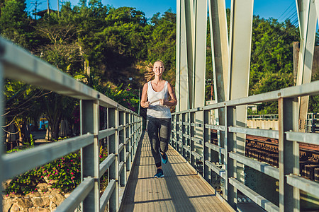 美丽的女人在日落时穿过桥过桥晴天太阳速度耐力训练慢跑者公园赛跑者男人耀斑图片
