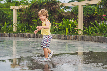 小男孩跑过水坑 夏天在户外靴子乐趣公园童年金发衣服孩子幼儿园行动孩子们图片
