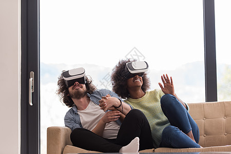 使用虚拟现实耳机的多种族夫妇乐趣眼镜房间男人电子游戏活动黑色手表技术沙发图片