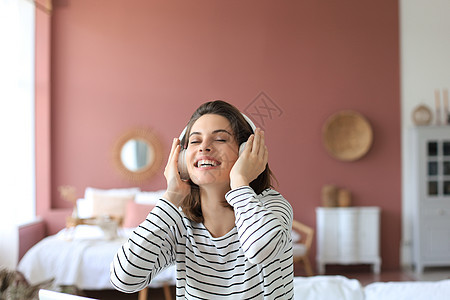 坐在沙发上的耳机里的美丽的黑头发女人 闭着眼睛听音乐享受快乐长椅黑发女性青年技术女士乐趣房间图片