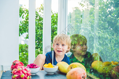 小可爱男孩在阳台上吃芒果异国幸福叶子快乐温泉闲暇微笑假期热带情调图片