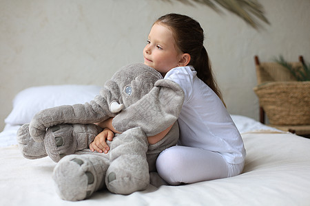 甜美的小女孩坐在她床上 在家中与玩具大象苏醒枕头微笑小憩房间女孩拥抱女性孩子卧室图片