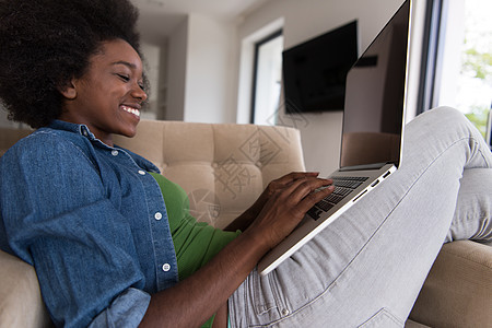 在家里使用笔记本电脑坐在椅子上的非裔美洲妇女棕色书柜奢华公寓化妆品客厅学生互联网沙发成人图片