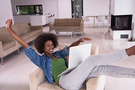 在家里使用笔记本电脑坐在椅子上的非裔美洲妇女化妆品监视器互联网沙发长椅女性闲暇黑发棕色扶手图片