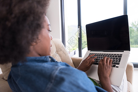 在家里使用笔记本电脑坐在椅子上的非裔美洲妇女活动沙发技术公寓成人互联网扶手棕色闲暇黑发图片