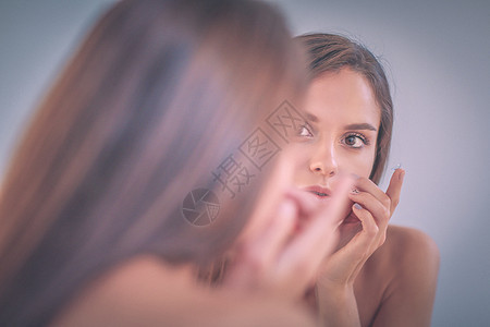 迷人的年轻女人在脸上涂奶油肤色洗漱卫生白色化妆品润肤护理反射镜子皮肤图片