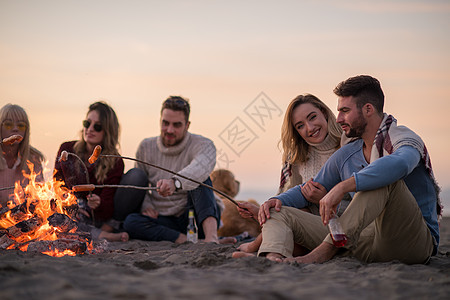 坐在海滩火炉边的年轻朋友团体靴子乐趣朋友们烹饪啤酒青年电话友谊烧烤假期图片