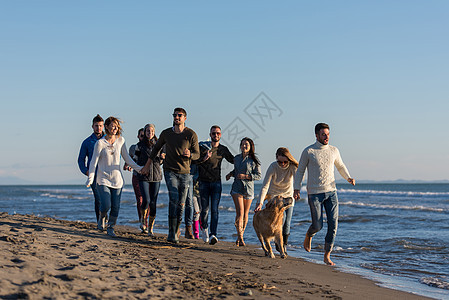 秋天在海滩上奔跑的一群朋友女性幸福海岸线海岸休闲鹅卵石情侣跑步帽子朋友们图片