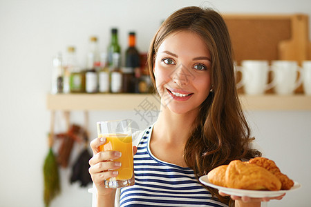 年轻女人拿着一杯果汁和蛋糕 站在厨房里图片