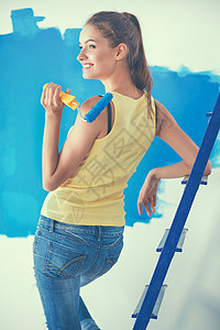 快乐的年轻美女 在墙壁上画画 站在梯子旁边图片