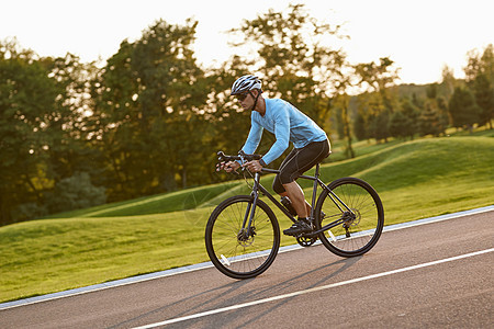 日落时分 一位身穿运动服的年轻运动员 职业自行车赛车手在城市公园骑山地公路自行车的侧视图图片