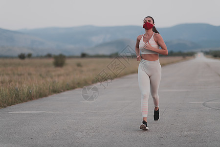 在冠状病毒爆发期间 穿着短衣 戴着红色防护面罩在城市户外跑步的坚定健身女性 Covid 19 和体育慢跑活动运动和健身预防感染疾图片