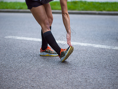 女士鞋女跑者在上午训练前升温和伸展运动员赛跑者女孩有氧运动森林跑步公园女性手表慢跑者背景