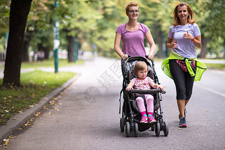 父母旅行女婴与婴儿婴儿婴儿车一起慢跑妈妈运动员精力运动快乐城市母性跑步家庭活动背景