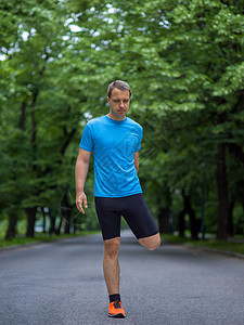 男子在上午训练前升温和伸展的男性跑者慢跑者身体森林公园赛跑者手表城市有氧运动运动跑步图片