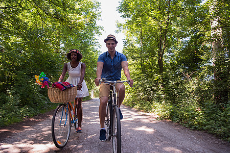 具有自然骑自行车的多种族年轻夫妇男人女性公园娱乐男生活动闲暇运动乐趣森林图片