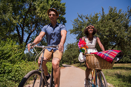 具有自然骑自行车的多种族年轻夫妇运动城市活动骑术森林娱乐公园女士成人男人图片