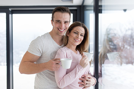 年轻夫妇在窗边享受清晨咖啡家庭财产奢华窗户亲热房子男人房间恋人拥抱图片