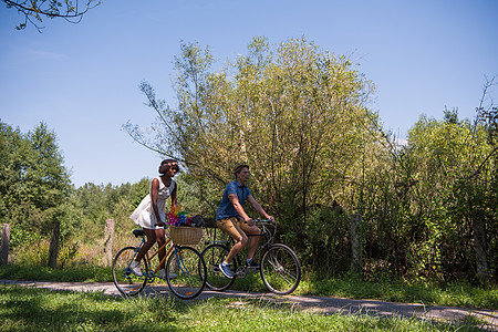 具有自然骑自行车的多种族年轻夫妇农村男生运动成人男性活动骑术天空乐趣公园图片