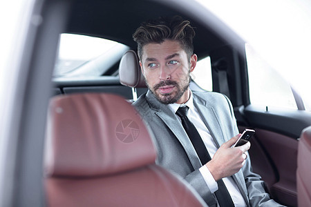 穿着西装的男子坐在车上 在智能手机上阅读信息图片